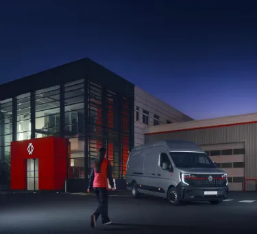 Une collaboratrice en tenue de service devant un Renault Trucks Master Red EDITION à la tombée de la nuit. Cette scène souligne la disponibilité des équipes et l'engagement du service client lors d'horaires d'accueil étendus en concession.