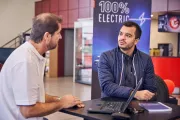 A dealer and a customer are discussing in front of a banner 100% electric